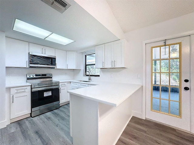 kitchen featuring kitchen peninsula, stainless steel appliances, light hardwood / wood-style floors, sink, and white cabinets