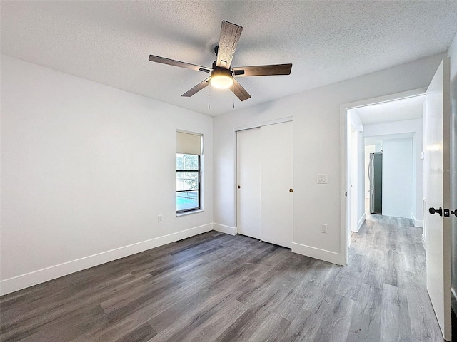 unfurnished bedroom featuring stainless steel fridge, a closet, ceiling fan, a textured ceiling, and hardwood / wood-style floors