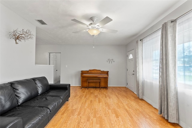 living room featuring baseboards, light wood finished floors, visible vents, and a ceiling fan