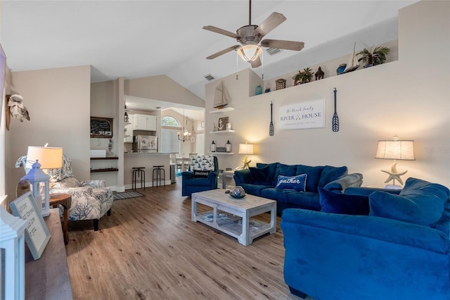 living area with visible vents, vaulted ceiling, light wood-style flooring, and ceiling fan with notable chandelier