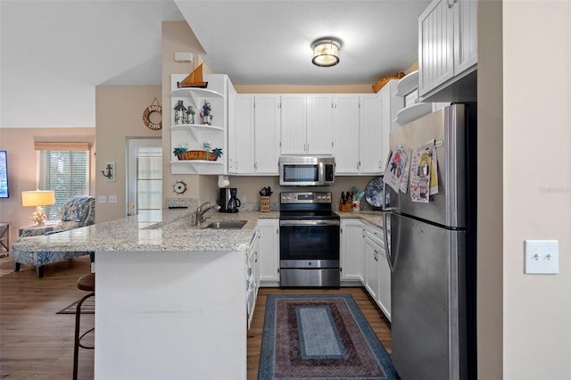 kitchen featuring a peninsula, a breakfast bar, a sink, white cabinetry, and appliances with stainless steel finishes