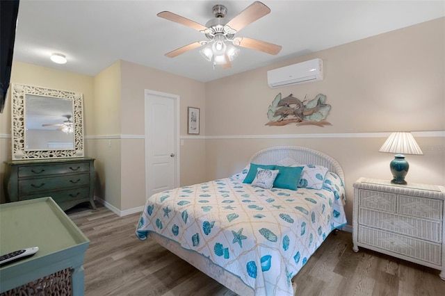 bedroom featuring ceiling fan, a wall mounted AC, wood finished floors, and baseboards