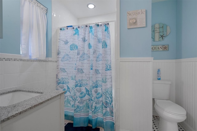 full bathroom featuring toilet, a shower with curtain, vanity, and wainscoting