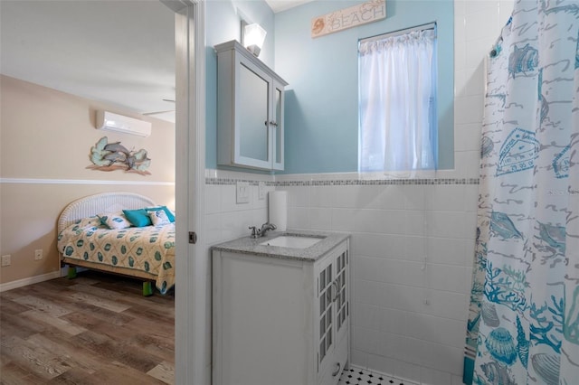 full bath featuring wood finished floors, ensuite bathroom, an AC wall unit, vanity, and tile walls