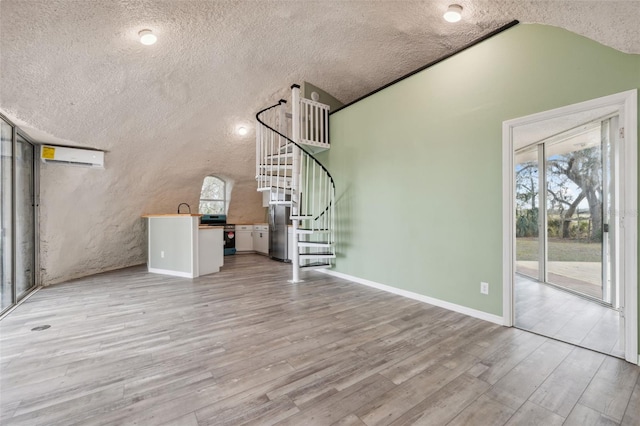 unfurnished living room with a wall mounted AC, vaulted ceiling, a textured ceiling, and light wood-type flooring