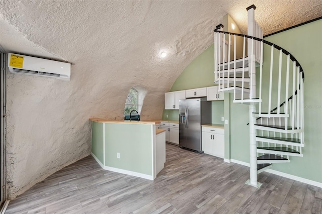 interior space featuring light hardwood / wood-style floors, vaulted ceiling, a wall unit AC, white cabinetry, and stainless steel fridge with ice dispenser