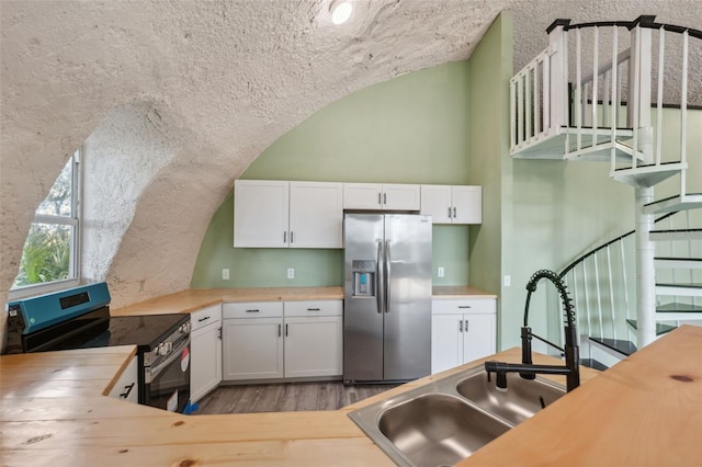 kitchen with appliances with stainless steel finishes, vaulted ceiling, sink, butcher block countertops, and white cabinets