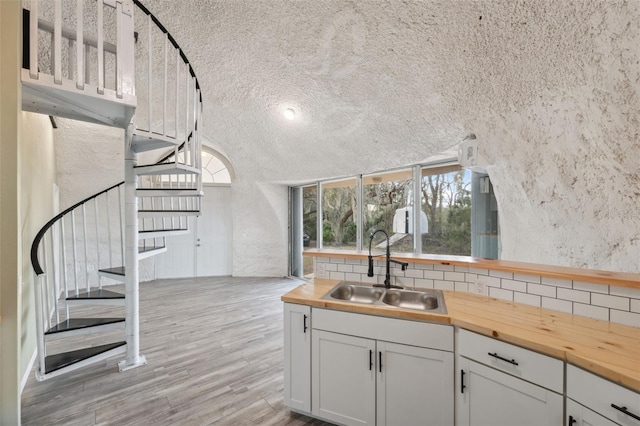 kitchen featuring white cabinetry, light hardwood / wood-style flooring, butcher block counters, sink, and backsplash