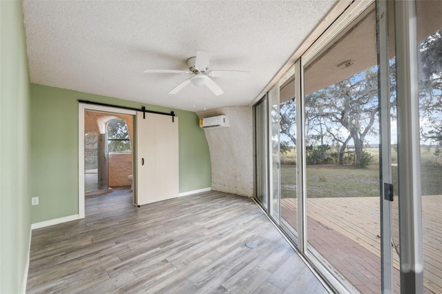 unfurnished sunroom with ceiling fan, a wall mounted AC, and a barn door