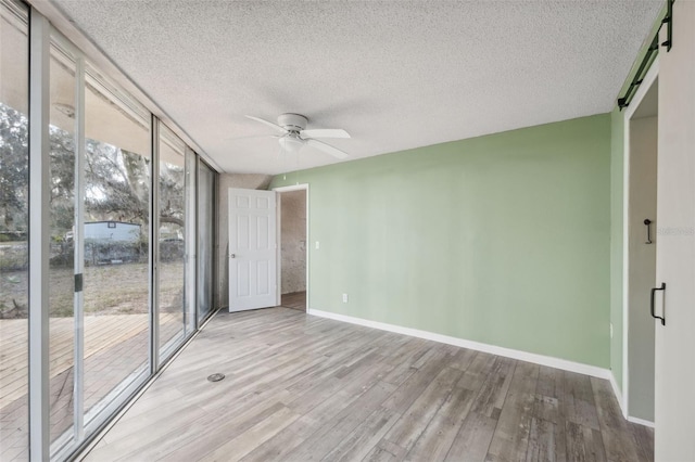 unfurnished room featuring light hardwood / wood-style flooring, a textured ceiling, ceiling fan, floor to ceiling windows, and a barn door