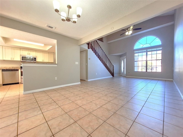 unfurnished living room with visible vents, stairway, light tile patterned flooring, baseboards, and ceiling fan with notable chandelier