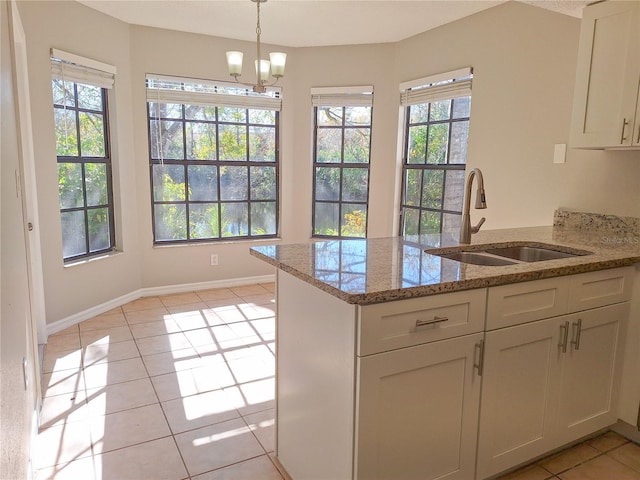 kitchen with light tile patterned floors, white cabinets, a sink, light stone countertops, and a peninsula