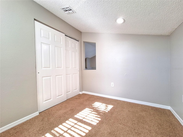 unfurnished bedroom featuring a closet, visible vents, carpet flooring, a textured ceiling, and baseboards