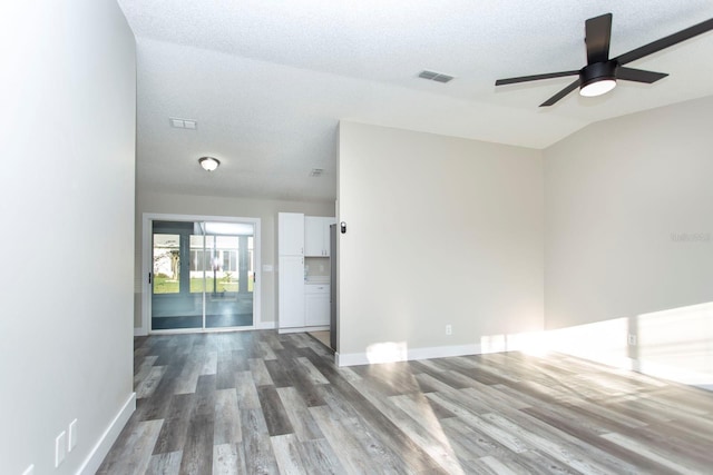 unfurnished room featuring a textured ceiling, lofted ceiling, dark wood-type flooring, visible vents, and baseboards