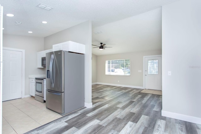 kitchen featuring lofted ceiling, appliances with stainless steel finishes, white cabinets, a textured ceiling, and baseboards