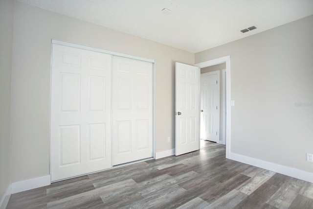 unfurnished bedroom featuring a closet, wood finished floors, visible vents, and baseboards