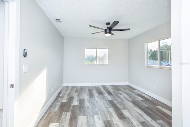 unfurnished room with visible vents, wood finished floors, a wealth of natural light, and baseboards