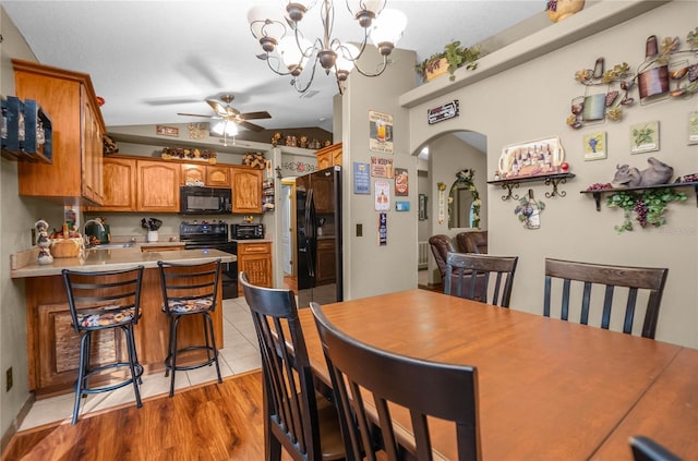 dining room with ceiling fan with notable chandelier, sink, light hardwood / wood-style floors, and lofted ceiling