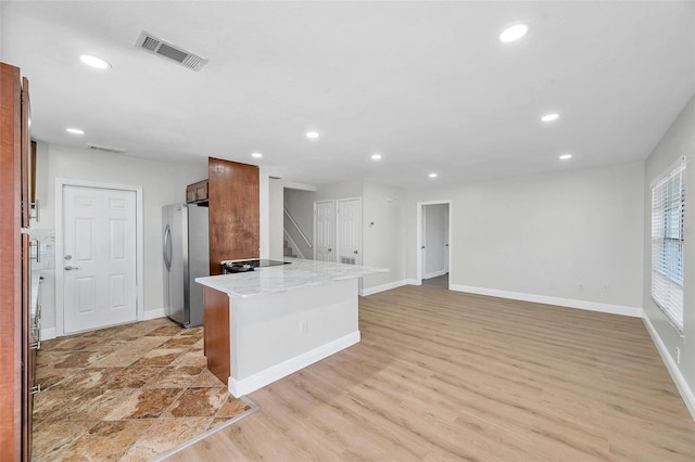 kitchen with light wood-type flooring, light stone countertops, and stainless steel fridge