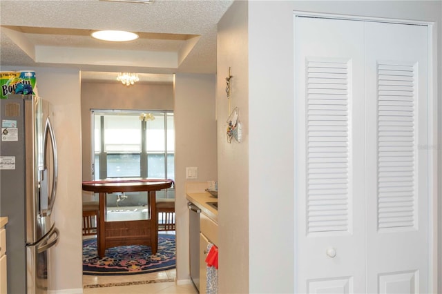 interior space featuring a raised ceiling, stainless steel appliances, a notable chandelier, and a textured ceiling