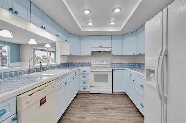 kitchen featuring white appliances, tile counters, white cabinets, under cabinet range hood, and a sink