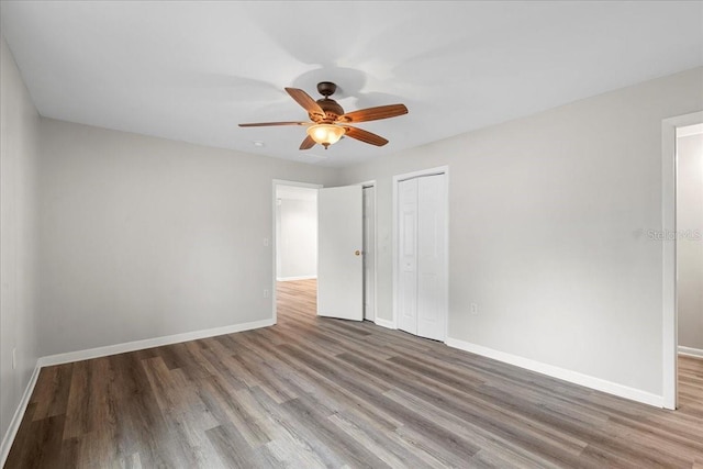 unfurnished bedroom with hardwood / wood-style floors, two closets, and ceiling fan