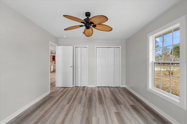 unfurnished bedroom with multiple windows, light hardwood / wood-style flooring, ceiling fan, and multiple closets