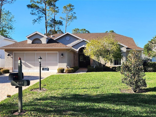 view of front of property featuring a garage, a shingled roof, brick siding, decorative driveway, and a front lawn