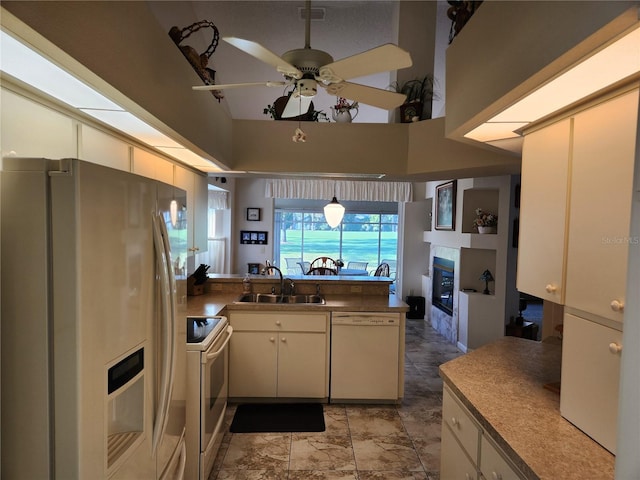 kitchen with a peninsula, white appliances, a sink, dark countertops, and a glass covered fireplace