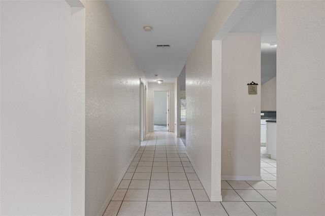 corridor with a textured wall, light tile patterned flooring, visible vents, and baseboards