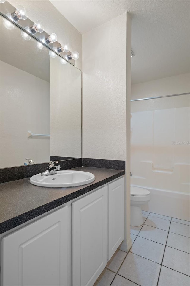 full bath featuring toilet, vanity, a textured ceiling, and tile patterned floors