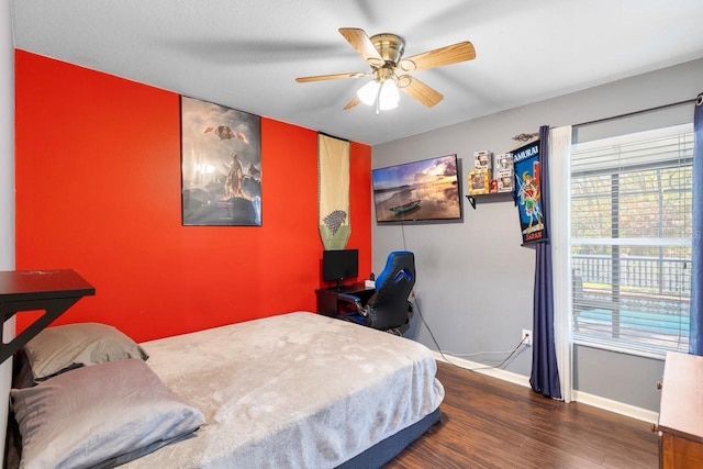 bedroom featuring ceiling fan, an accent wall, baseboards, and dark wood finished floors