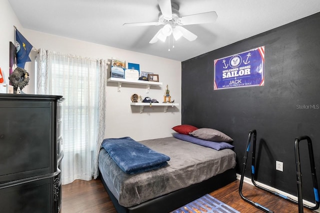 bedroom featuring an accent wall, a ceiling fan, and dark wood-type flooring