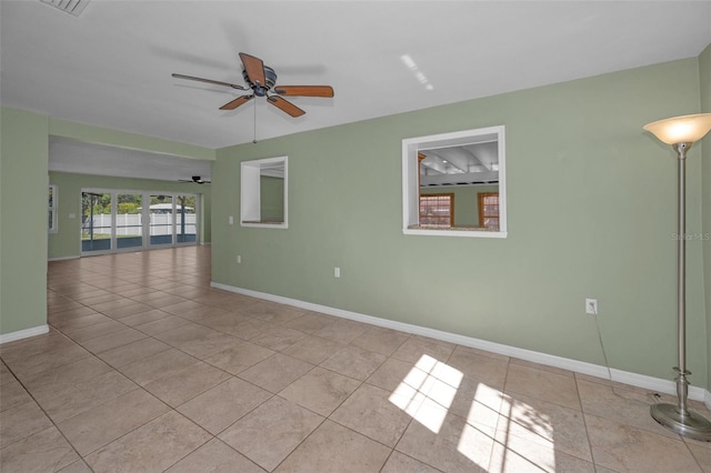 tiled empty room featuring a ceiling fan and baseboards