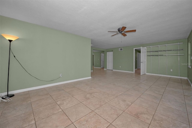 spare room featuring light tile patterned floors, visible vents, a ceiling fan, a textured ceiling, and baseboards