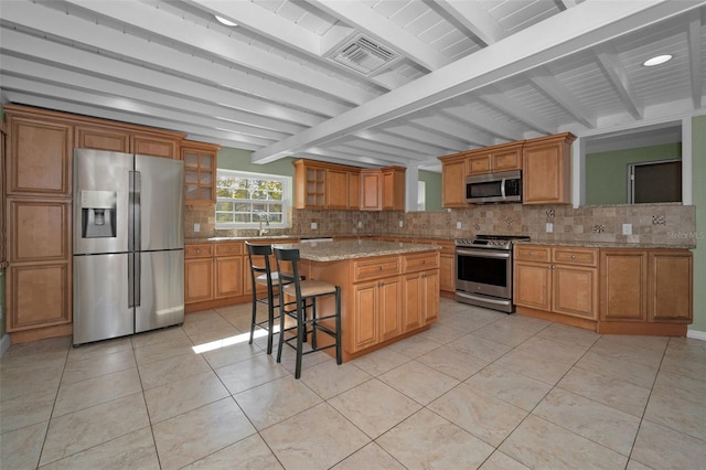 kitchen with a center island, light tile patterned floors, tasteful backsplash, appliances with stainless steel finishes, and a kitchen bar