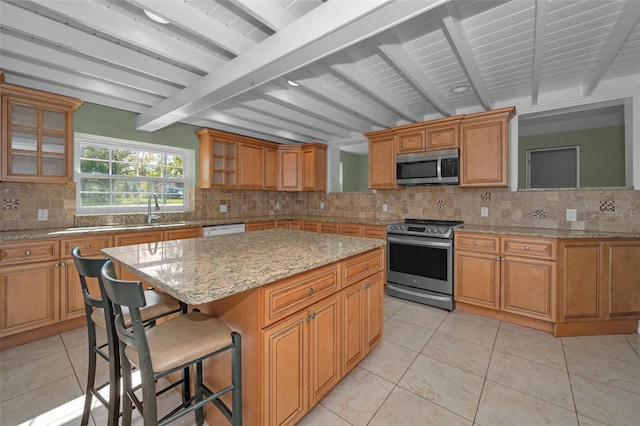 kitchen with stainless steel appliances, a kitchen island, a kitchen breakfast bar, beam ceiling, and tasteful backsplash