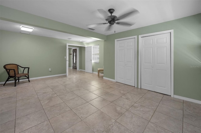 unfurnished bedroom with light tile patterned floors, a ceiling fan, baseboards, visible vents, and multiple closets