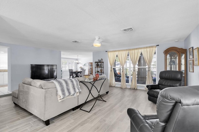 living room with visible vents, a notable chandelier, a textured ceiling, and light wood finished floors