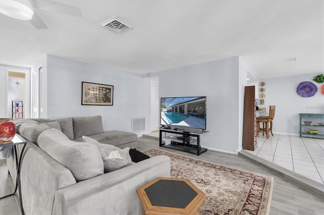 living room with light wood-type flooring, ceiling fan, visible vents, and baseboards