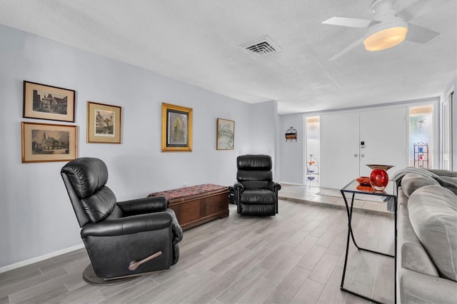 living room with light wood-type flooring, visible vents, a textured ceiling, and baseboards