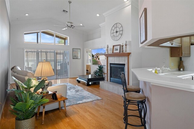living area featuring crown molding, light wood-style floors, ceiling fan, a tiled fireplace, and visible vents