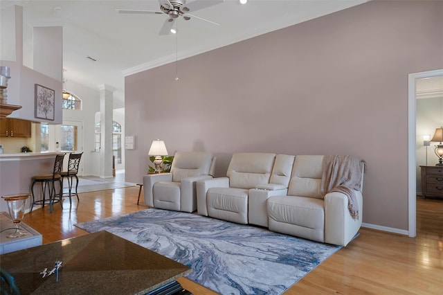 living area with crown molding, baseboards, a towering ceiling, a ceiling fan, and light wood-type flooring