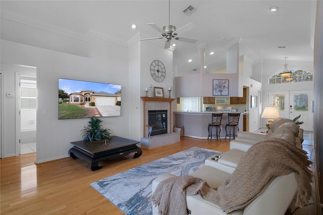living area featuring high vaulted ceiling, light wood-style flooring, visible vents, a fireplace, and a ceiling fan