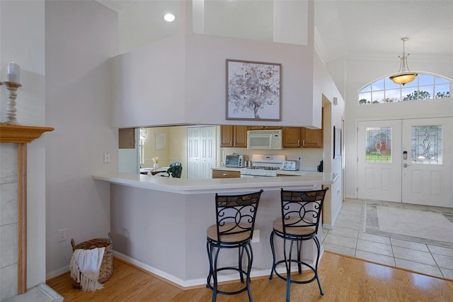 kitchen featuring high vaulted ceiling, light countertops, brown cabinets, and white appliances