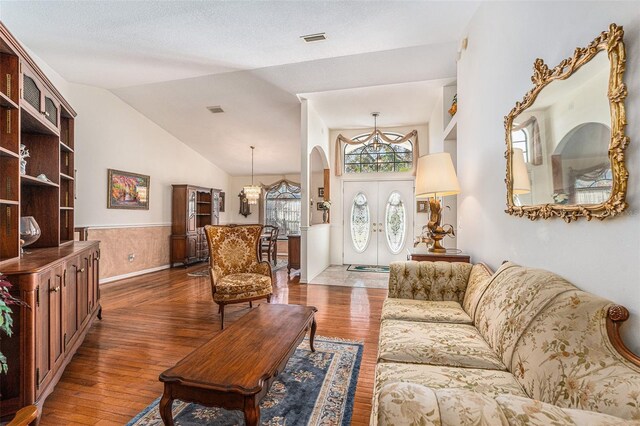 living room with dark wood-style flooring, a wainscoted wall, vaulted ceiling, and visible vents