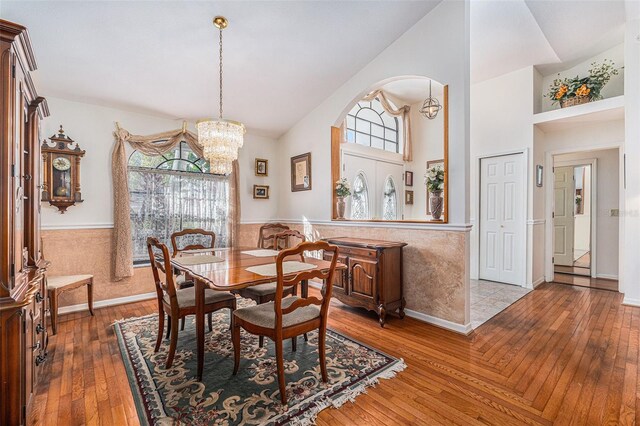 dining area featuring a chandelier, high vaulted ceiling, arched walkways, a wainscoted wall, and wood finished floors