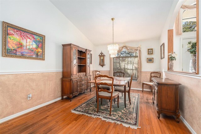 dining area featuring light wood-type flooring, a wainscoted wall, a chandelier, and high vaulted ceiling