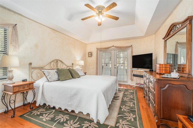 bedroom featuring ceiling fan, a tray ceiling, dark wood-style flooring, and french doors