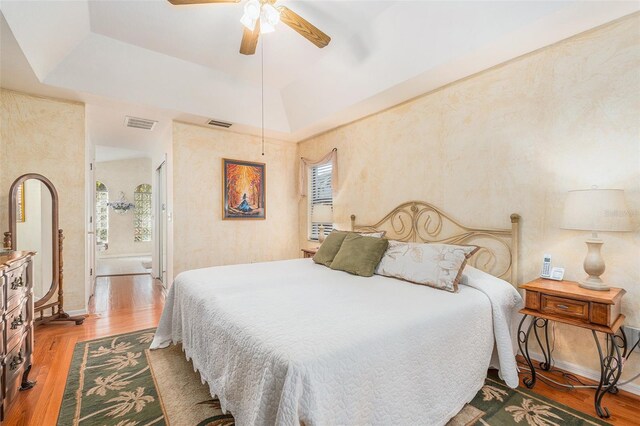 bedroom with a ceiling fan, a raised ceiling, visible vents, and wood finished floors